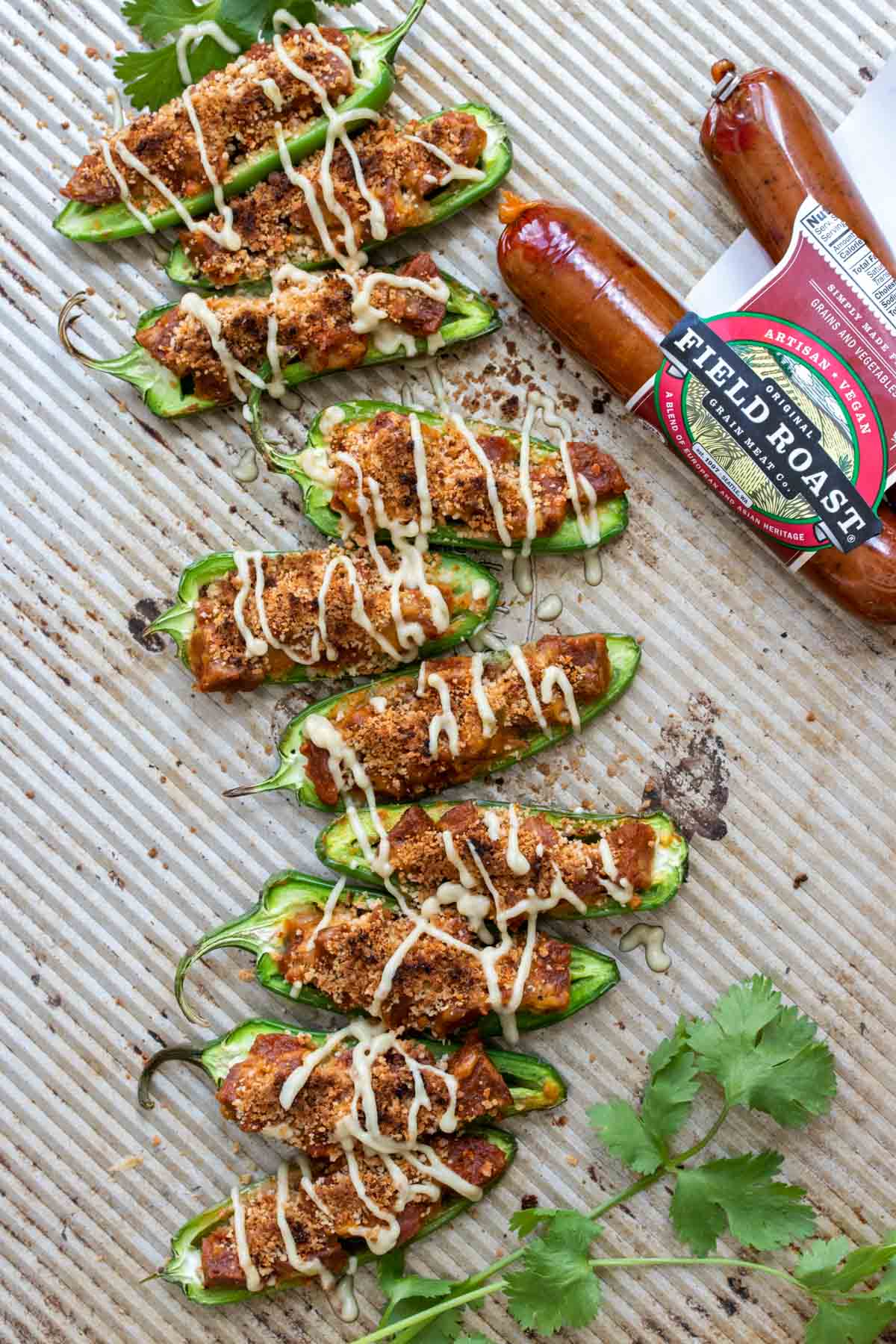 Baking sheet with stuffed jalapeños drizzled with cheese sauce next to package of sausages