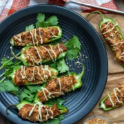 Top view of vegan sausage stuffed jalapeños drizzled with white cheese sauce on a black plate