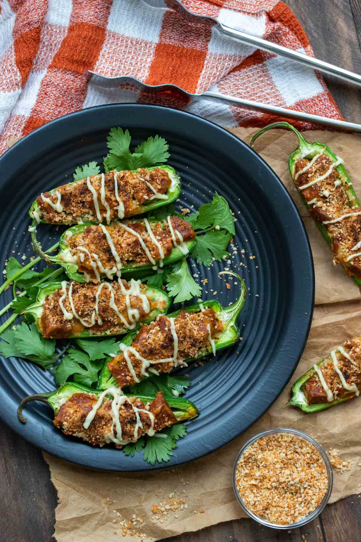 Top view of vegan sausage stuffed jalapeños drizzled with white cheese sauce on a black plate