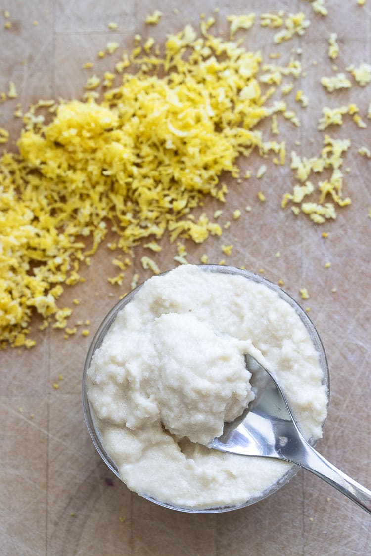 Spoon dipping into bowl filled with lemon ricotta next to pile of lemon zest