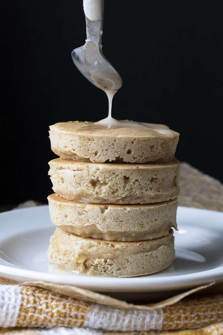 Spoon drizzling white lemon glaze on a stack of pancakes.