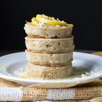 Stack of lemon ricotta pancakes topped with lemon slices, powdered sugar and glaze