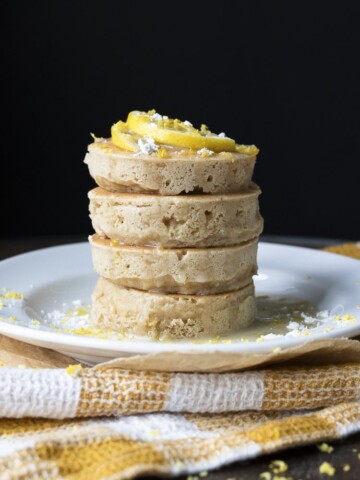 Stack of lemon ricotta pancakes topped with lemon slices, powdered sugar and glaze