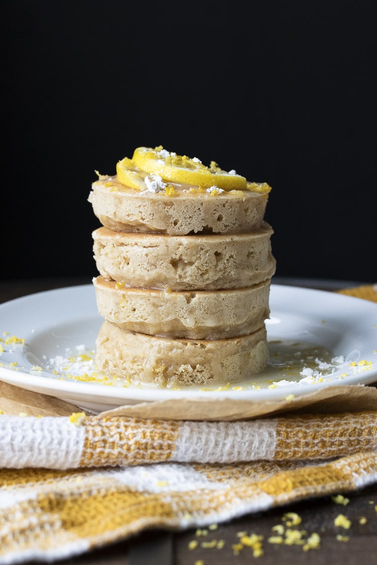 Stack of lemon ricotta pancakes topped with lemon slices, powdered sugar and glaze