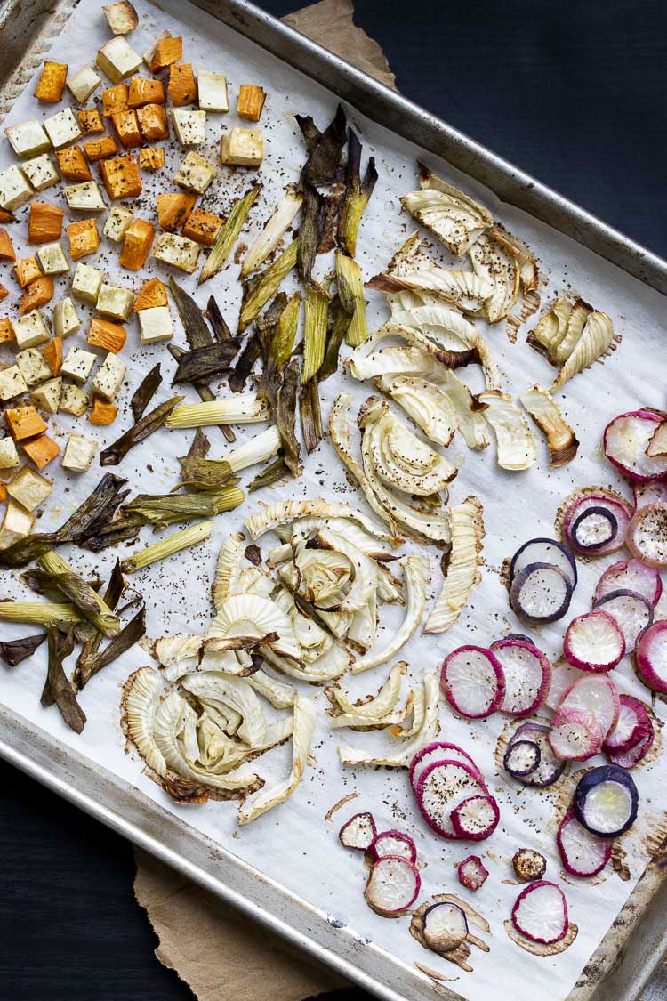 Roasted sweet potato, green onions, fennel bulb and radishes on a parchment lined baking sheet