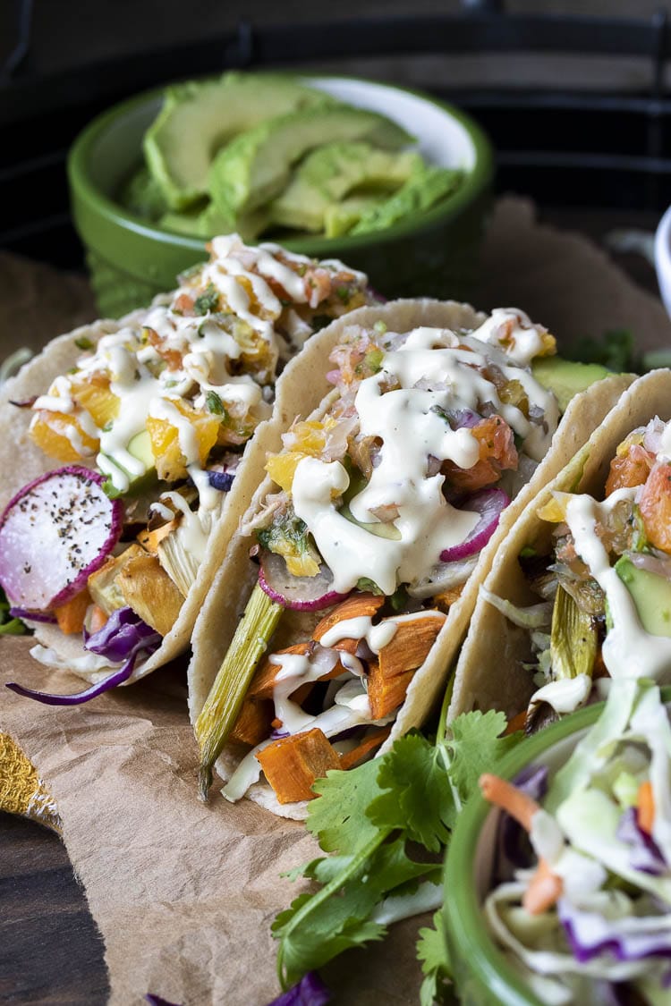 Front view of tacos filled with roasted veggies, citrus salsa, avocado and creamy sauce