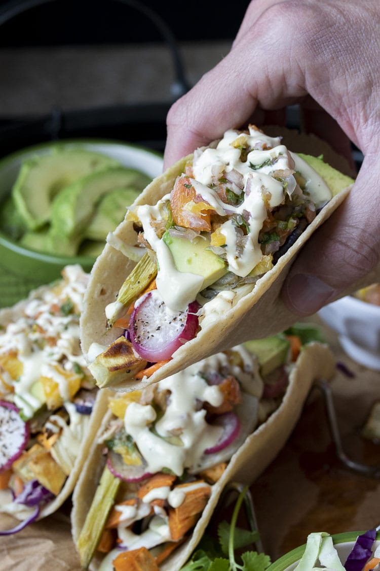 Hand picking up a roasted veggie taco with avocado, salsa and cream sauce