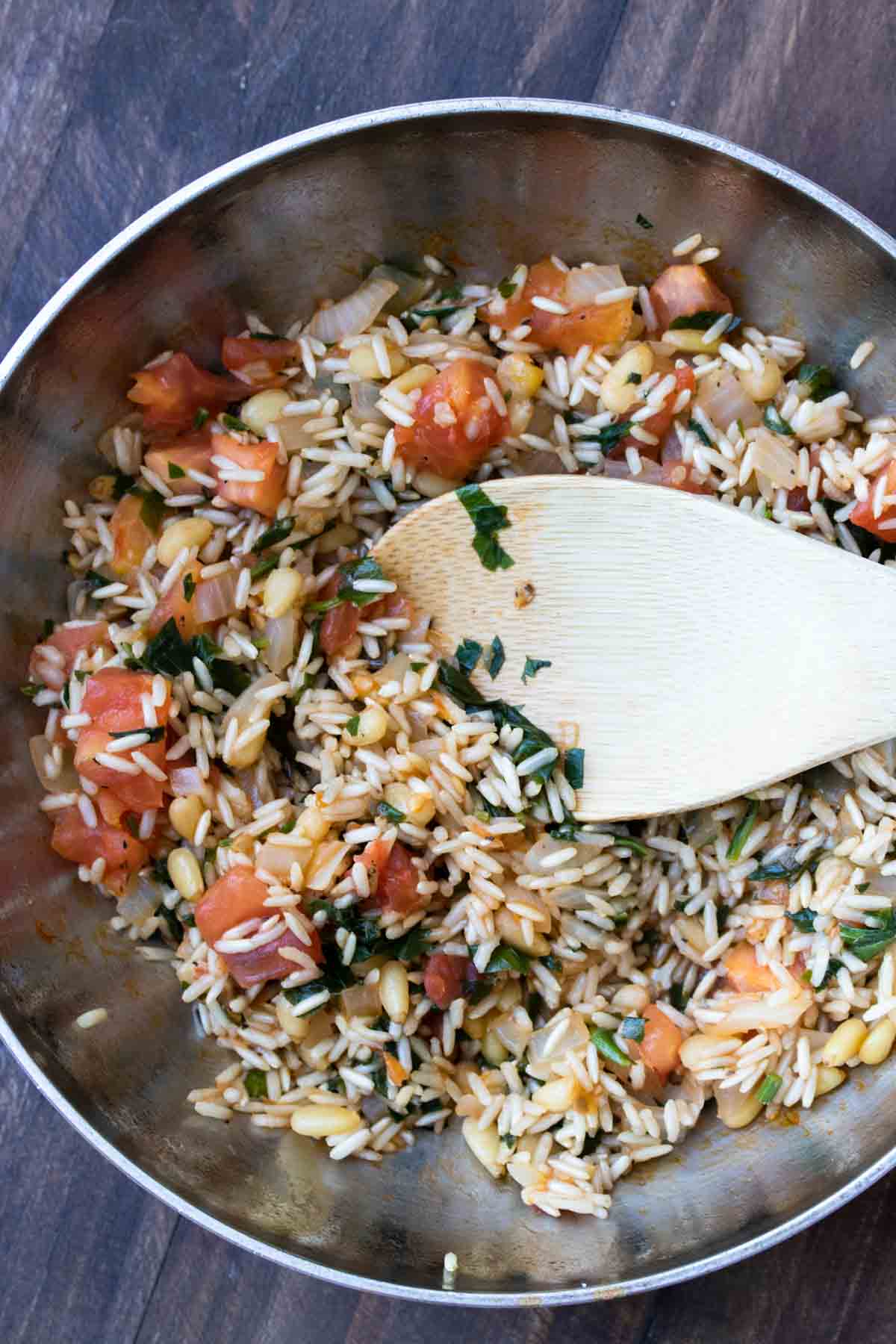 Wooden spoon stirring rice mixture cooking in a stainless steel pan