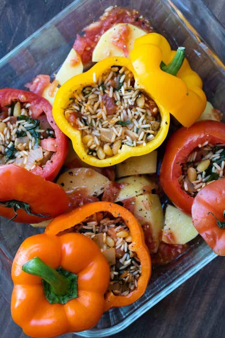 Peppers and tomatoes stuffed with rice mixture in a glass baking dish before being baked.
