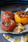 Stuffed tomatoes and peppers with potatoes on a parchment paper on a black plate.