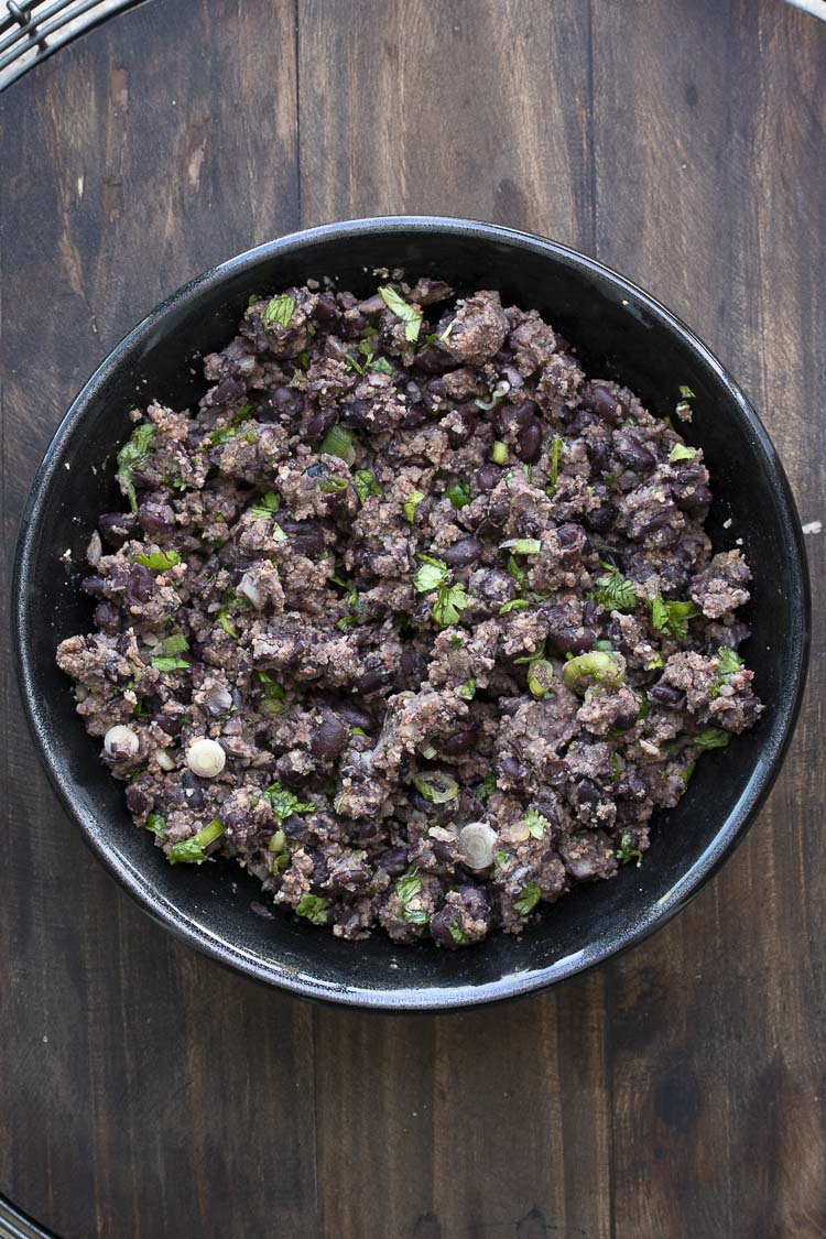 Black bowl filled with mashed black bean burger mixture and green onions