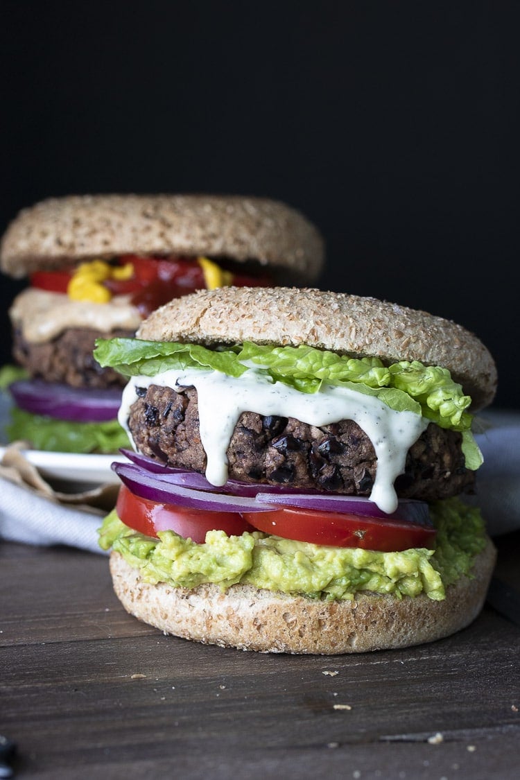 A black bean burger with lettuce, tomato, onions and guacamole on a wooden surface