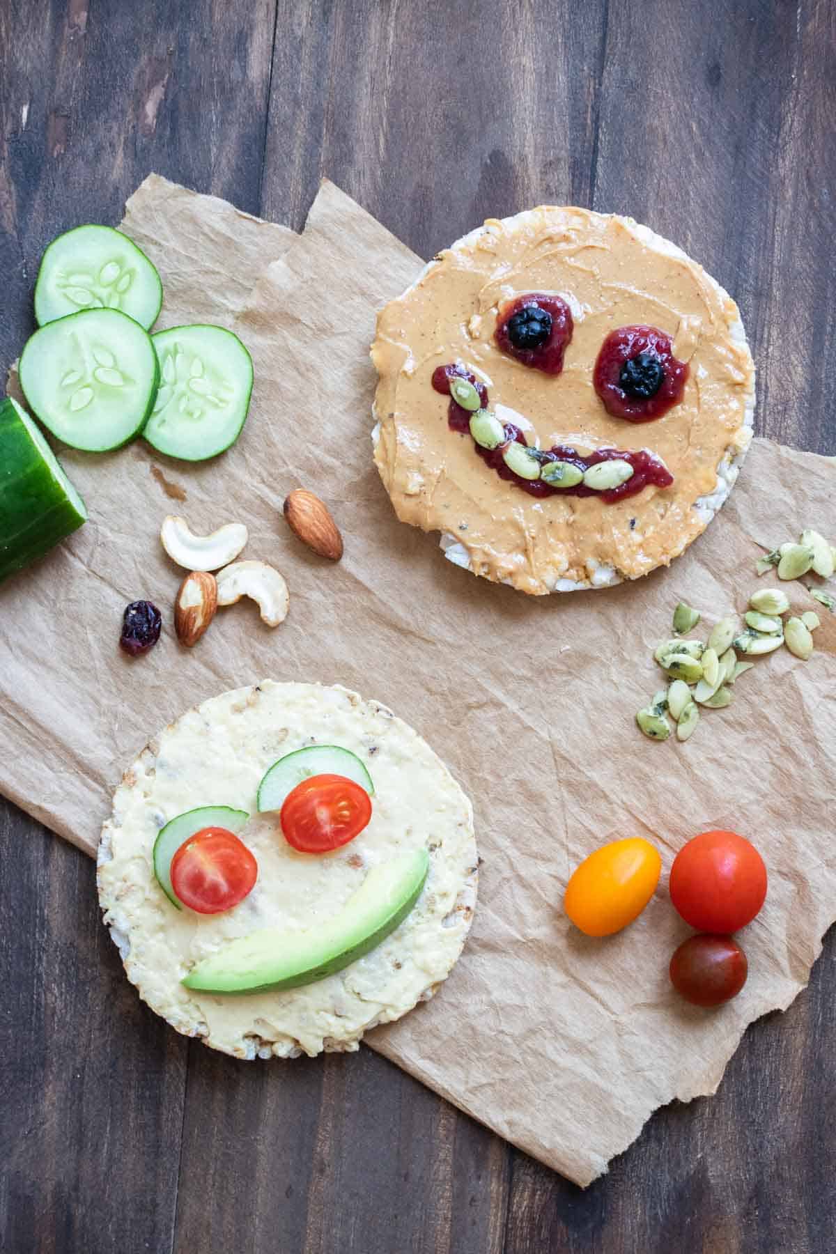 Rice cakes decorated as faces using nut butter, hummus, seeds, veggies, dried fruit and nuts