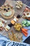 Food for a kids lunchbox like pizza, fruit, veggies and crackers on a piece of parchment paper on a blue towel.