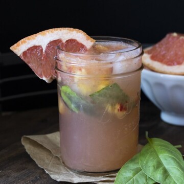 Glass mason jar filled with grapefruit juice, basil and chopped peaches on a wooden table