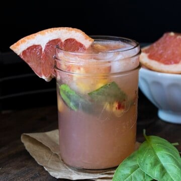 Glass mason jar filled with grapefruit juice, basil and chopped peaches on a wooden table