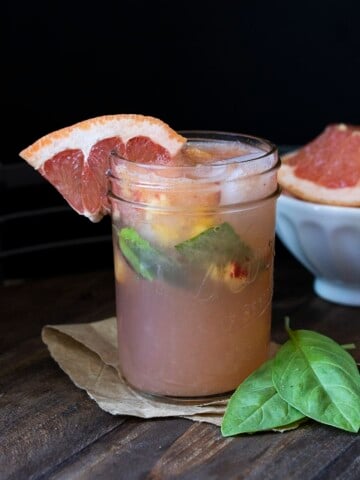 Glass mason jar filled with grapefruit juice, basil and chopped peaches on a wooden table