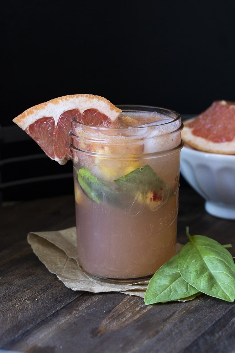 Glass mason jar filled with grapefruit juice, basil and chopped peaches on a wooden table