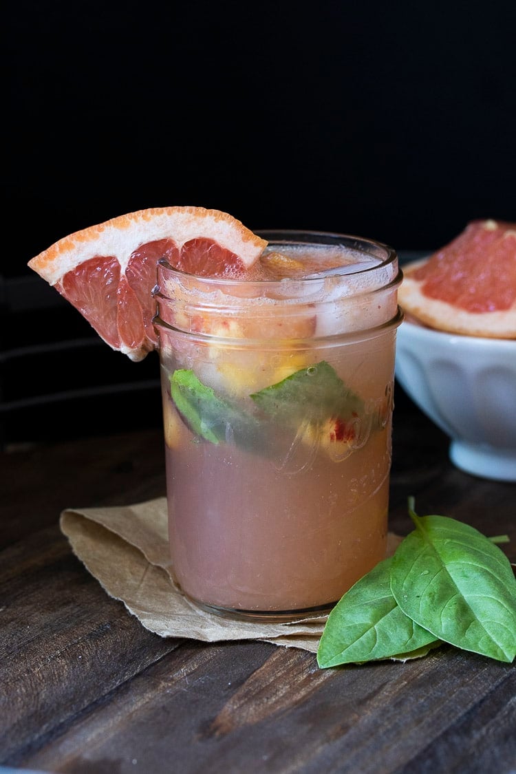 Glass mason jar filled with grapefruit juice, basil and chopped peaches on a wooden table