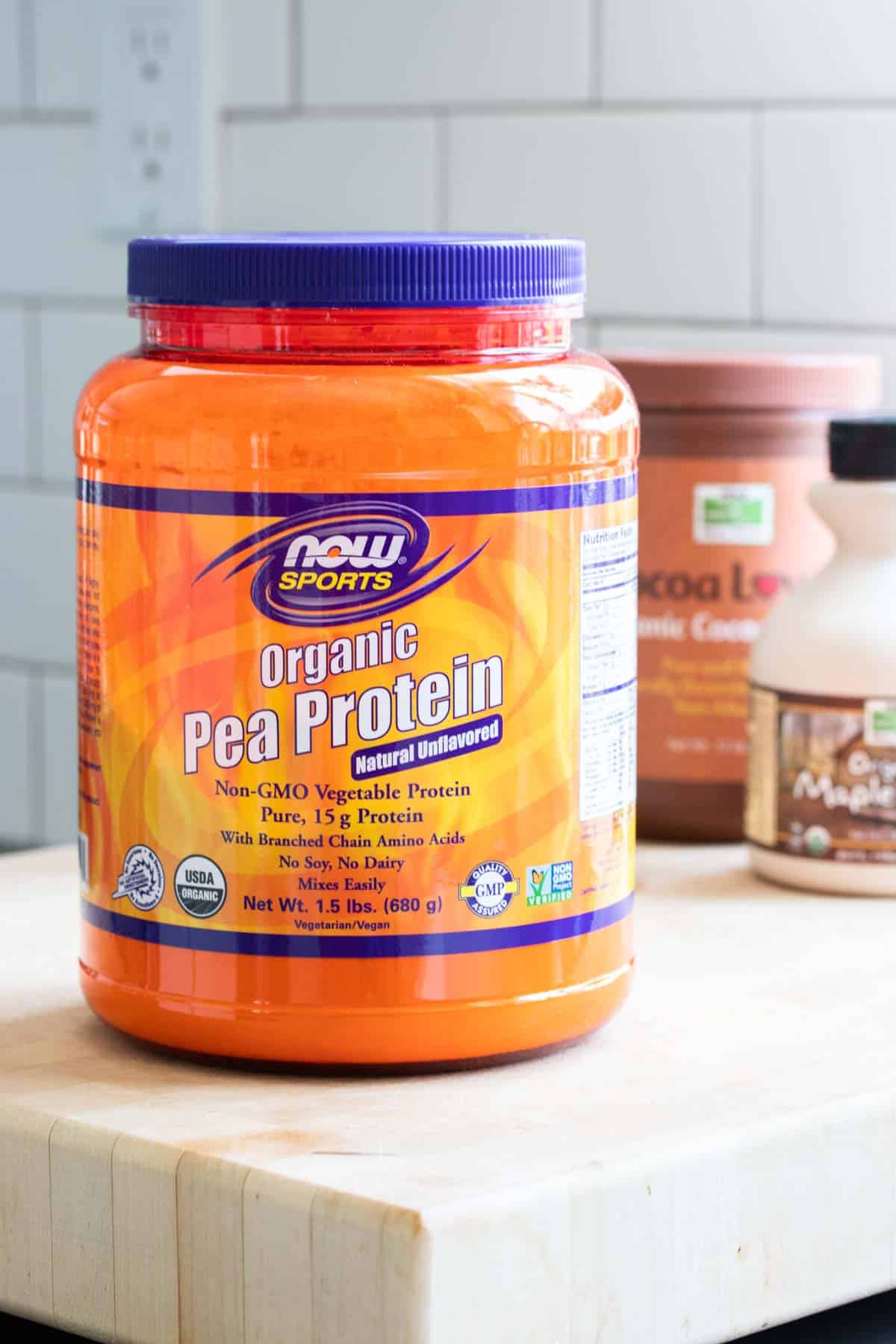 Orange NOW Sports pea protein powder container on a wood table