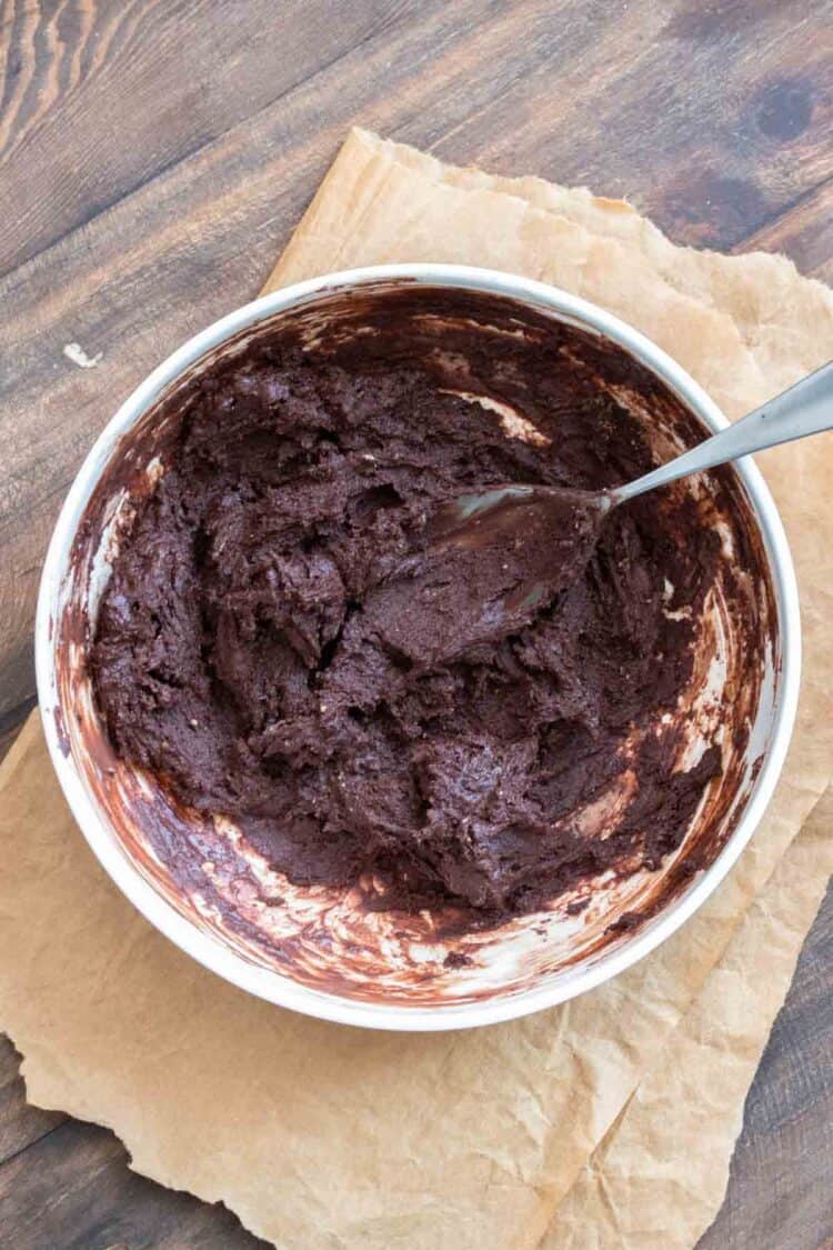 Spoon mixing brownie batter in a white bowl.