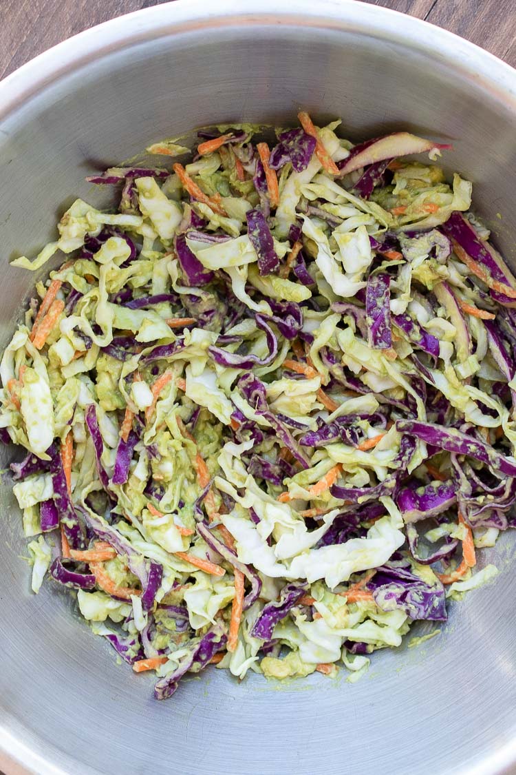 Shredded purple and green cabbage mixed with avocado in a silver bowl