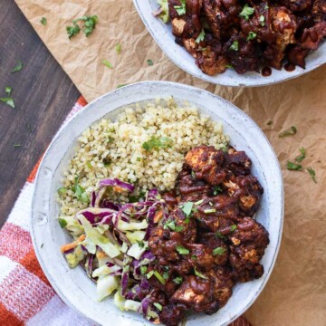 Top view of two white bowls with quinoa, cabbage slaw and BBQ cauliflower bites
