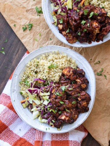 Top view of two white bowls with quinoa, cabbage slaw and BBQ cauliflower bites