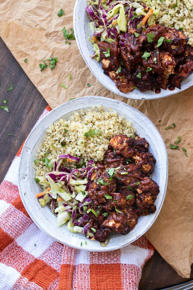 Top view of two white bowls with quinoa, cabbage slaw and BBQ cauliflower bites