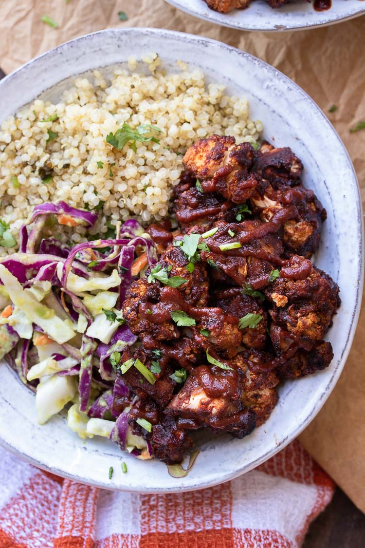 Close up of white bowl filled with BBQ cauliflower pieces, quinoa, and cabbage slaw