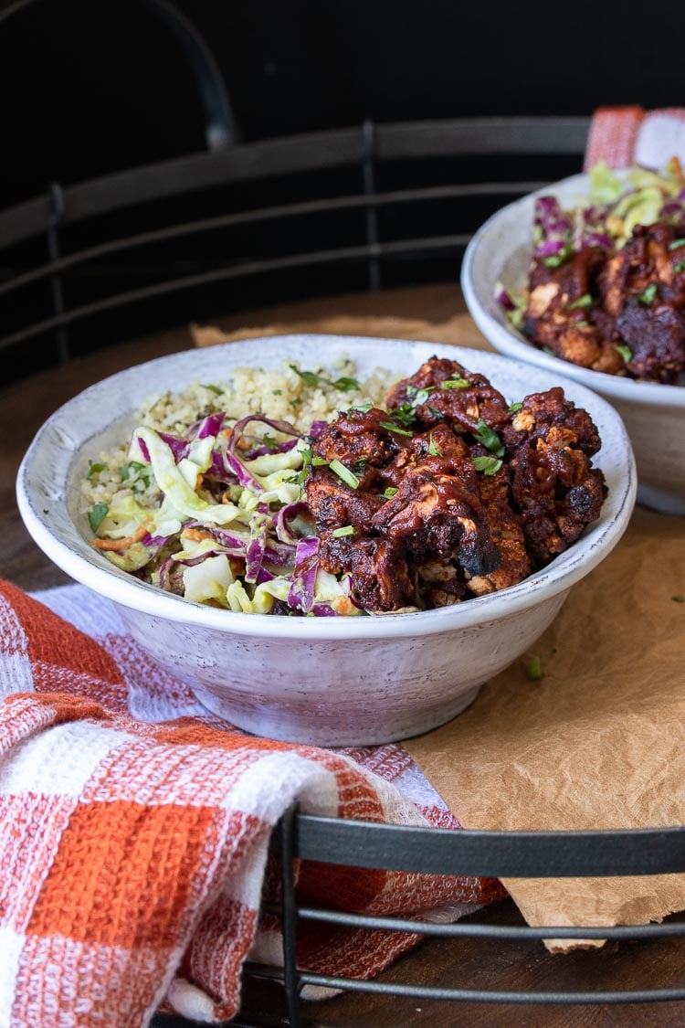 Front view of BBQ cauliflower bites, quinoa and cabbage slaw in two white bowls