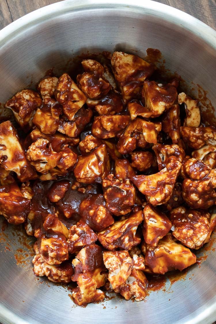 Pieces of cauliflower mixed with BBQ sauce in a silver bowl