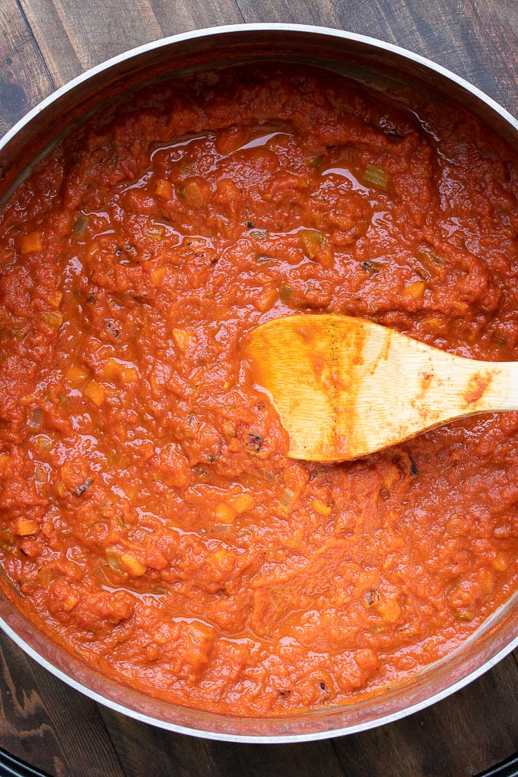 Wooden spoon stirring a chunky tomato sauce in a metal pan