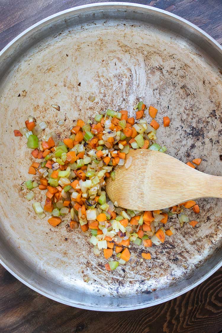 Wooden spoon browning celery, carrots and onion in a metal pan