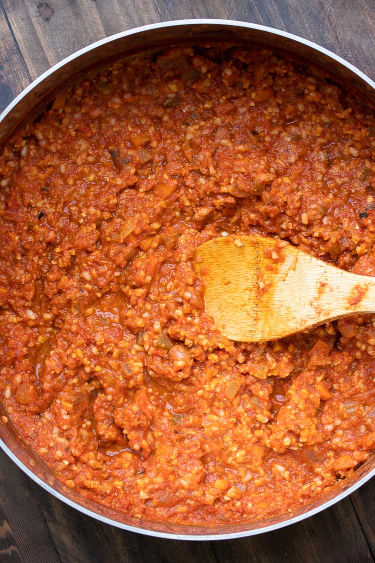 Meaty looking tomato sauce being stirred by a wooden spoon