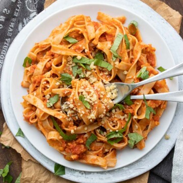 Long flat noodles mixed with meaty red sauce and topped with basil on a white plate