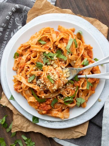 Long flat noodles mixed with meaty red sauce and topped with basil on a white plate