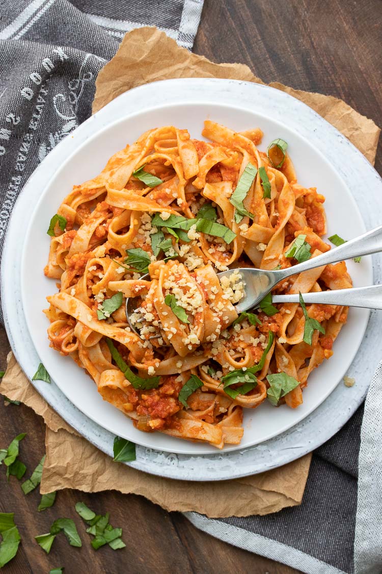 Long flat noodles mixed with meaty red sauce and topped with basil on a white plate