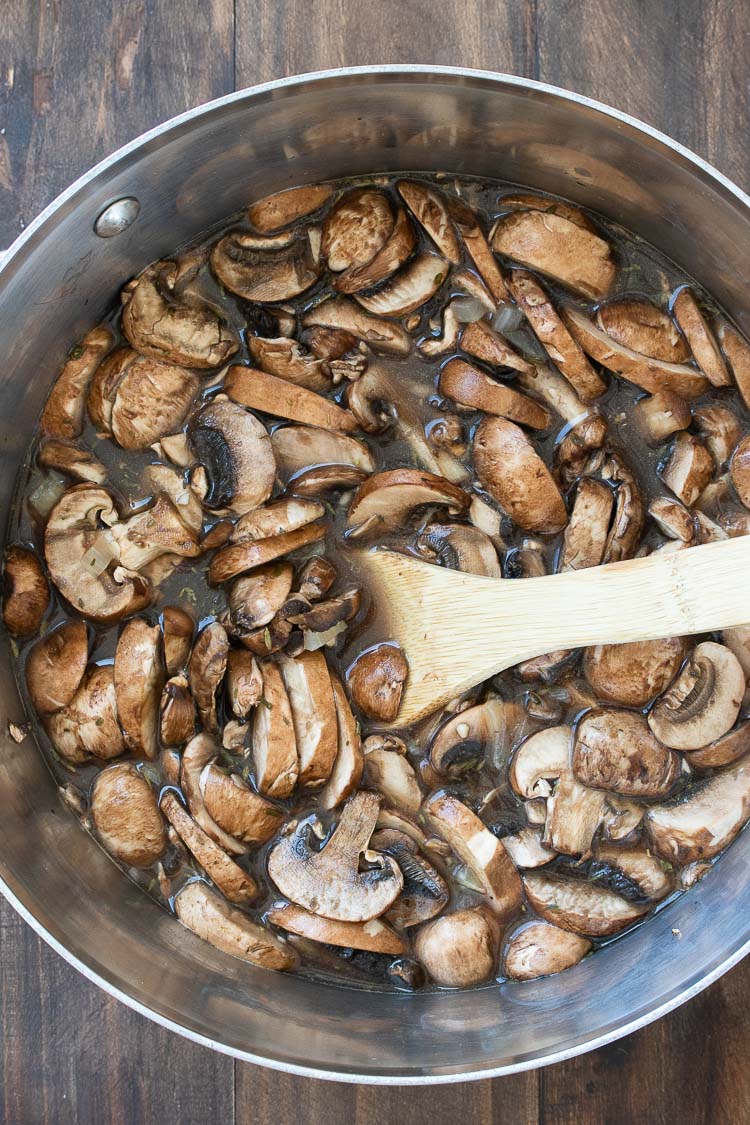 Wooden spoon mixing broth with sliced mushrooms in a metal pot