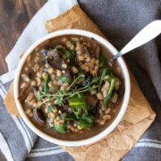 Top view of white bowl filled with a mushroom and barley stew with spinach and thyme