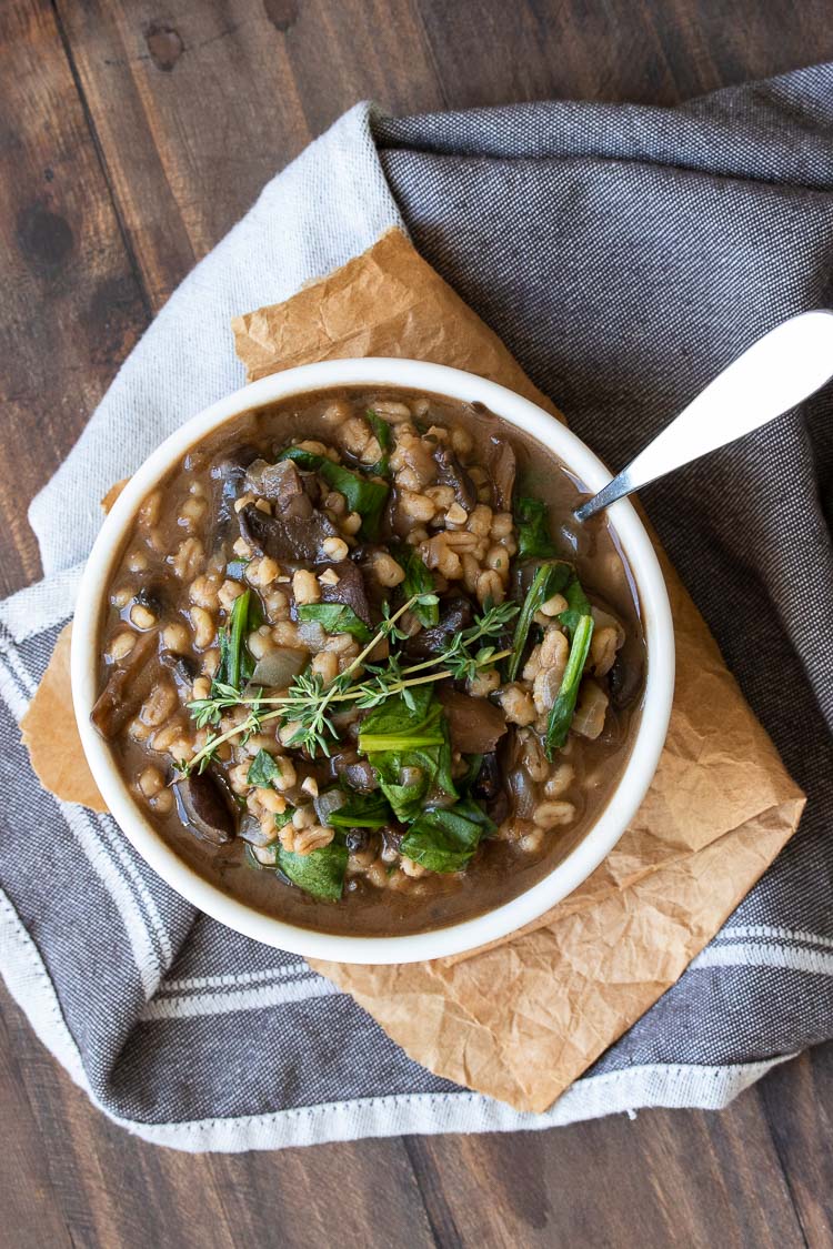 Top view of white bowl filled with a mushroom and barley stew with spinach and thyme