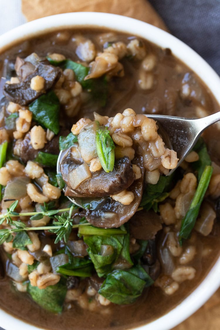 Metal spoon scooping out some barley, mushroom and spinach stew