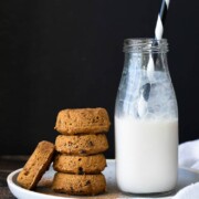 Stack of pumpkin donuts next to a jar of milk on a white plate