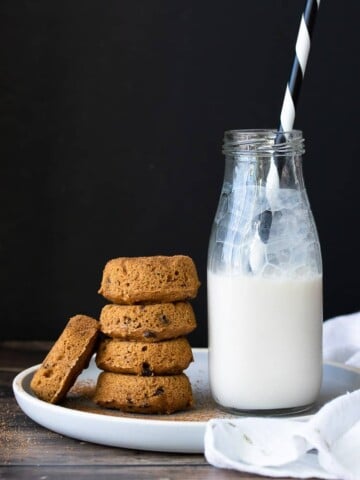 Stack of pumpkin donuts next to a jar of milk on a white plate