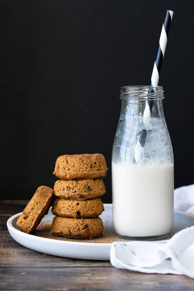 Stack of pumpkin donuts next to a jar of milk on a white plate