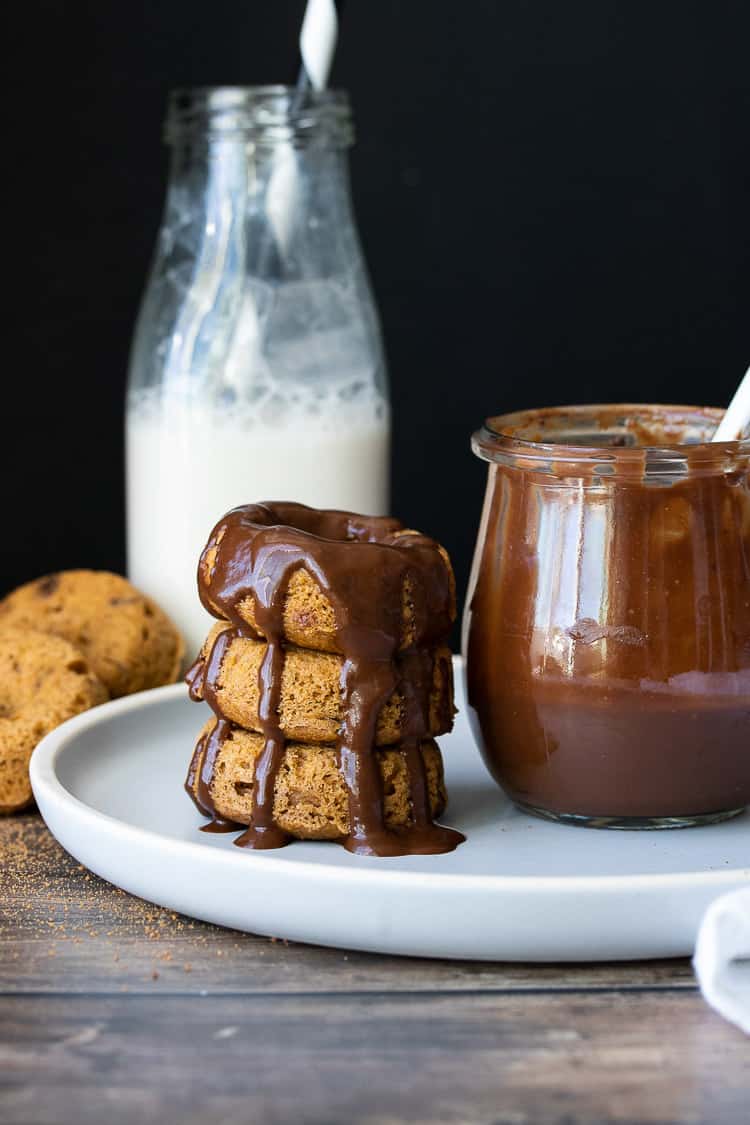 Stack of donuts covered in chocolate sauce next to a jar of chocolate sauce