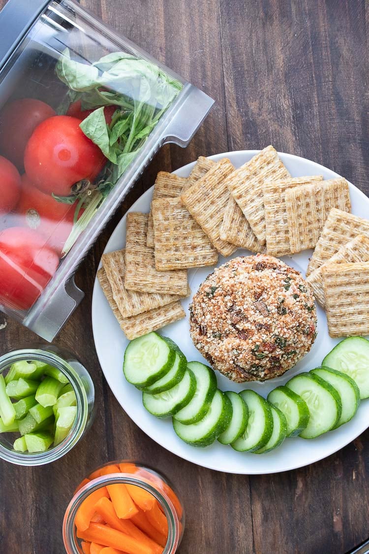 Top view of cheeseball on a white plate with crackers and cucumbers