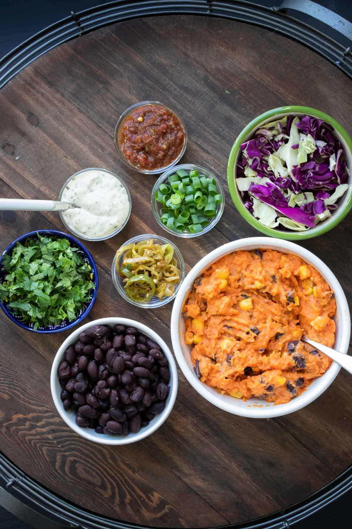 Top view of sweet potato mixture and potato skin toppings on a wooden tray.