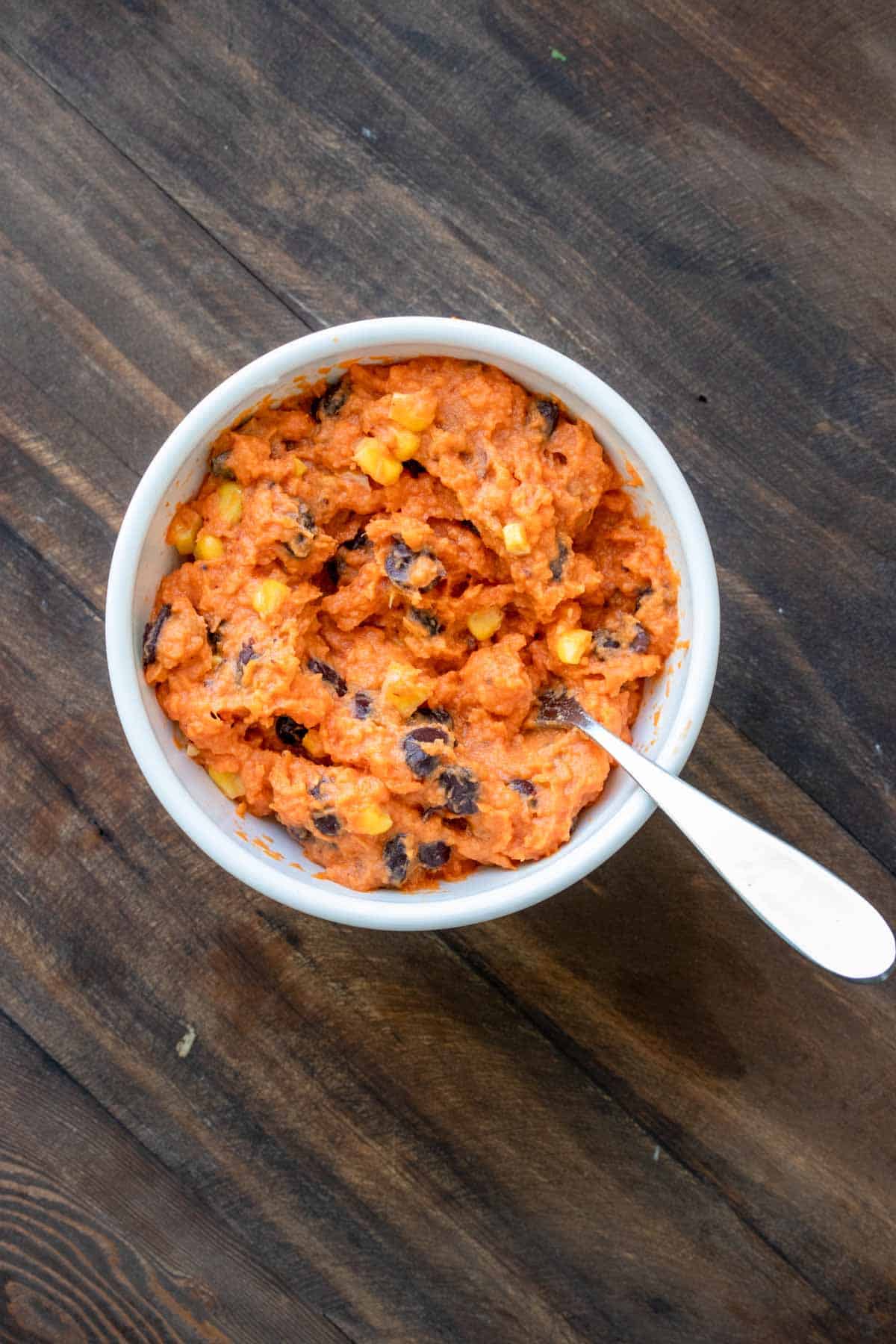 Top view of mashed sweet potato with black beans and corn in a white bowl