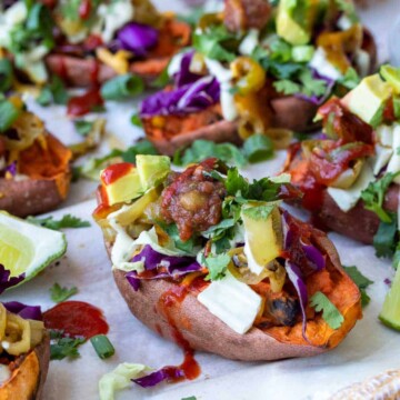 Front view of sweet potato skin loaded with toppings on white parchment